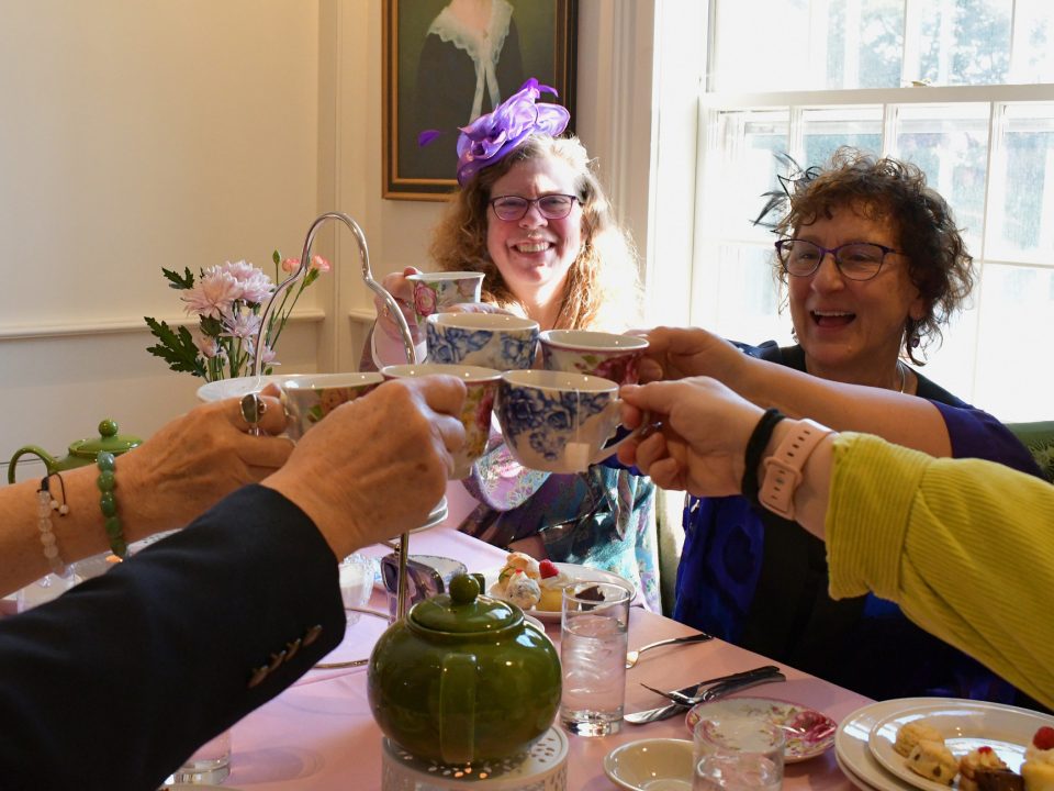 A group of people toast their tea while smiling