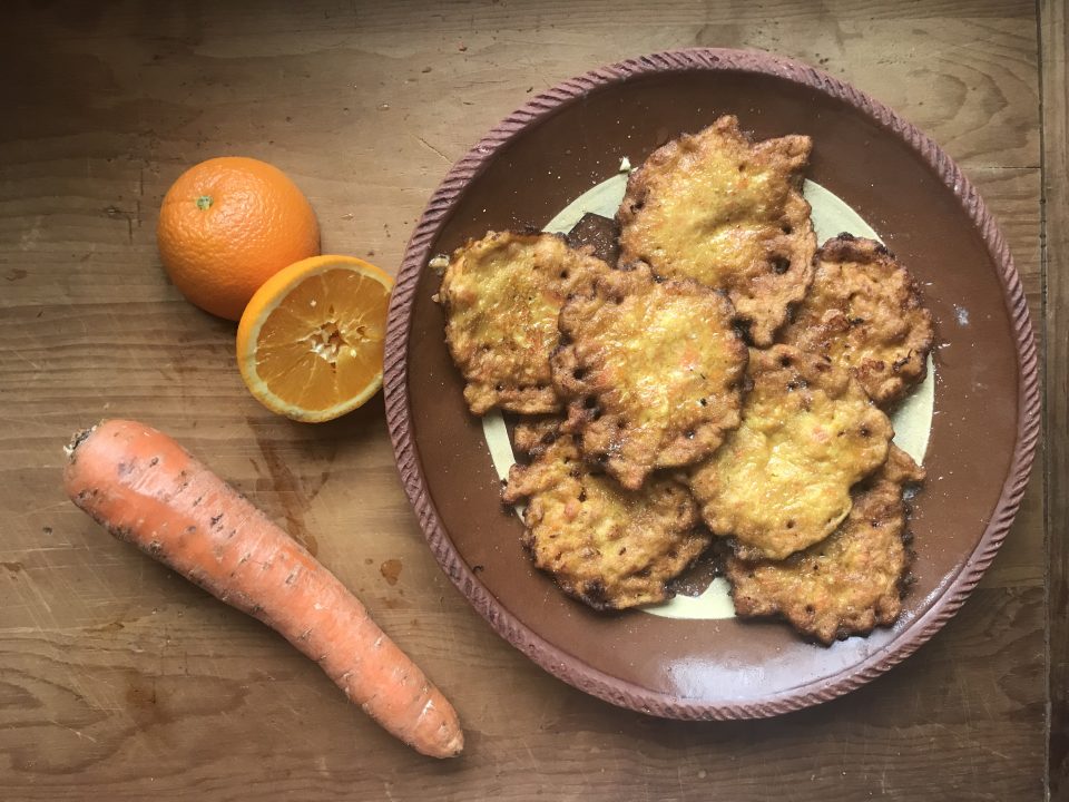 Finished carrot fritters on a plate with a carrot and orange on the side