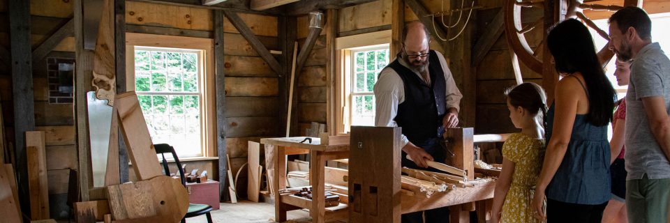 A family chats with a cabinetmaker in full 1830s costume