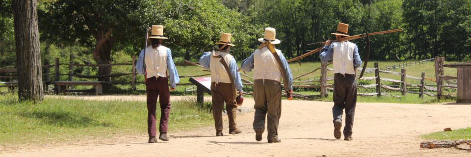 Four farmers in historical costume head out to the fields with their tools in tow