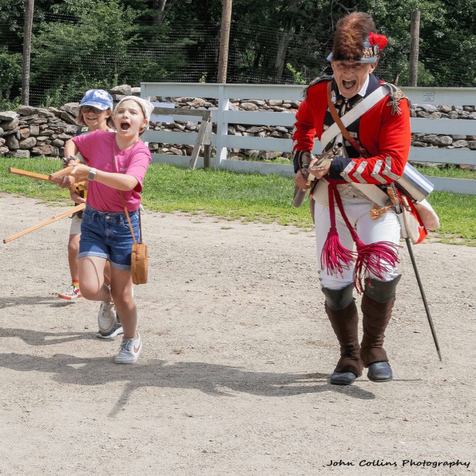Kids drilling with a man dressed as a British solider in the American Revolution